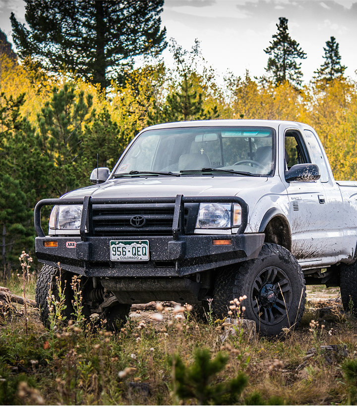 A front view of a Toyota Tacoma with Colorado number plates parked in the nature, mud splashed on itself.